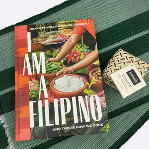 Kain Tayo features the cookbook "I Am a Filipino: And this is how we Cook" by Nicole Ponseca and Miguel Trinidad, 2 woven green placements, and 1 Ilocano salt